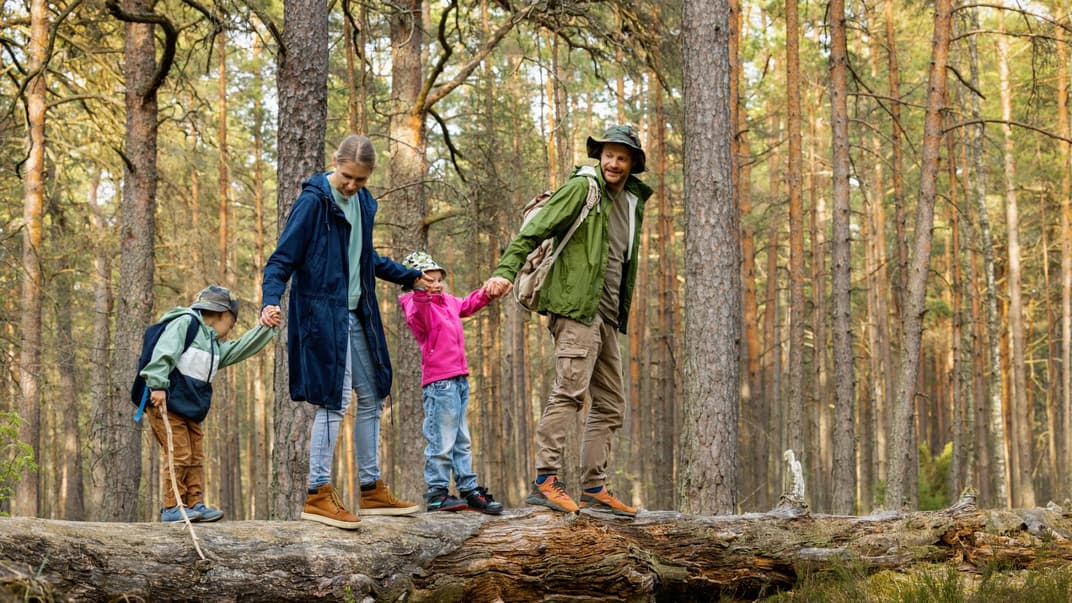 Familie läuft auf Baumstamm im Wald.