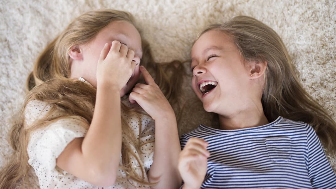 Zwei Mädchen liegen lachend auf dem Boden. 