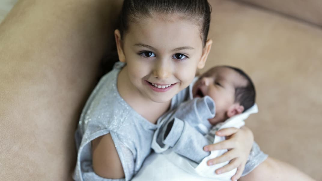 Mädchen hält Baby im Arm.
