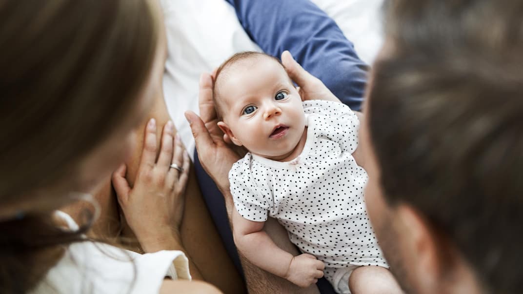 Mutter, Vater und Baby auf einem weißen Bett.