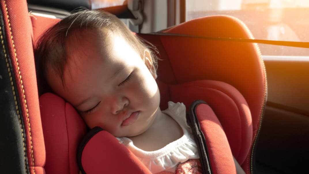 Müssen wir unsere Kinder im Auto wirklich mit Sonnencreme einschmieren? Ein Baby sitzt im Kindersitz des Autos, während die Sonne hereinscheint.