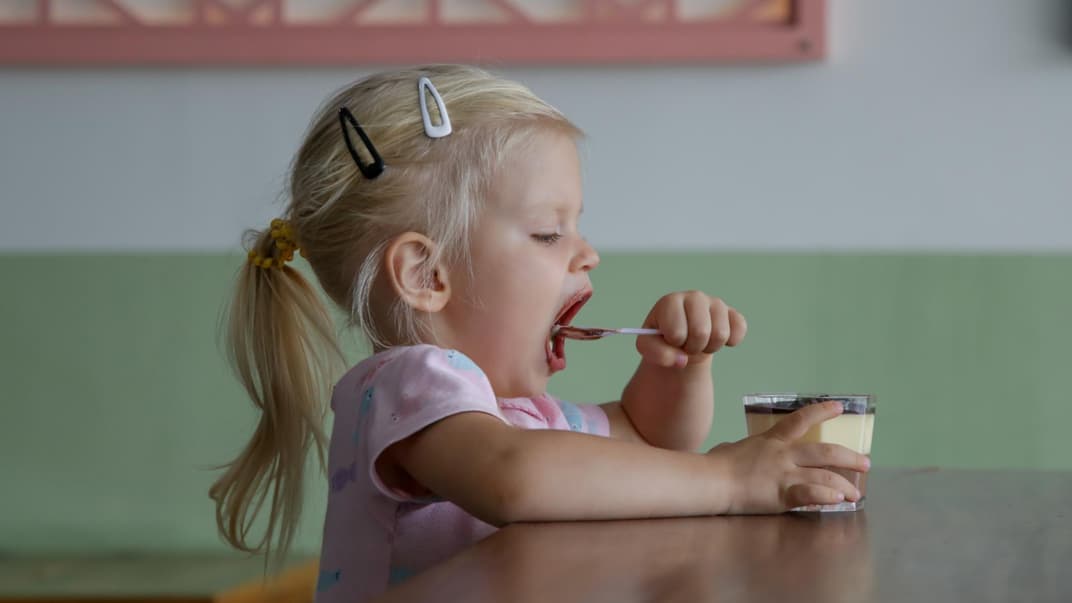 Kleines Mädchen löffelt Dessert. 
