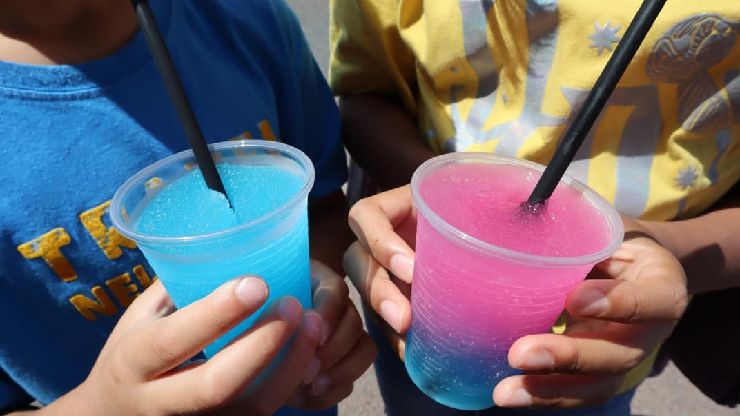 Zwei Kinder trinken rosa-blauen Slush. 