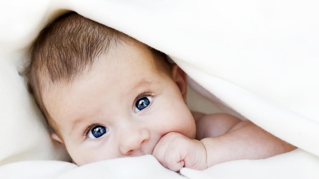 Baby guckt unter Decke hervor.