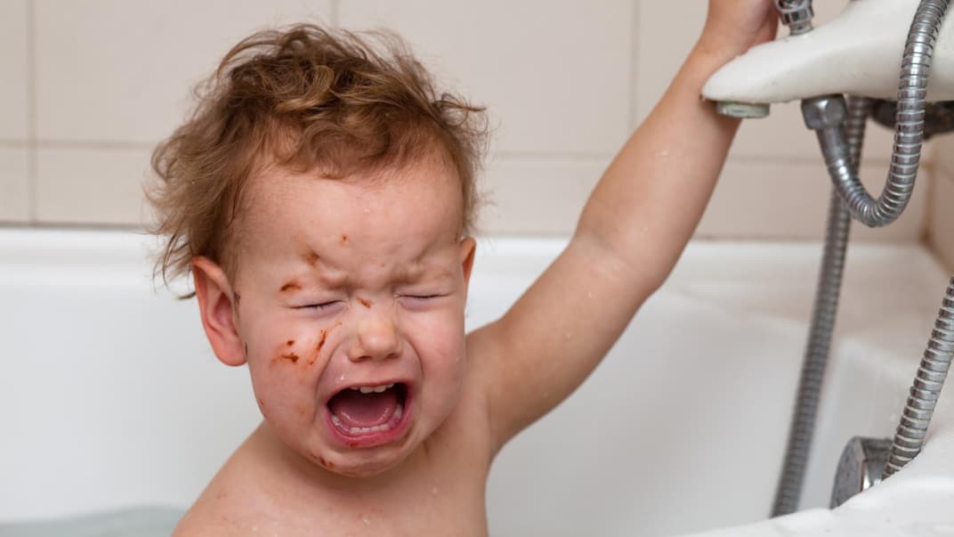 Ein Baby schreit beim Baden in der Badewanne und kneift dabei die Augen zu.