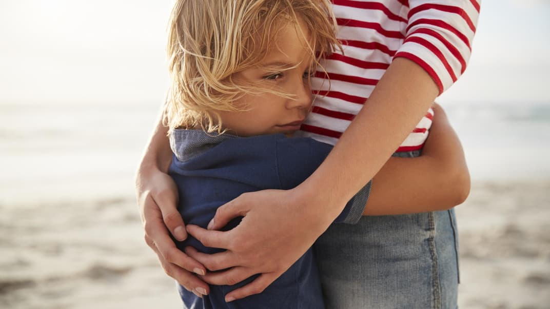 Mutter umarmt Sohn am Strand.