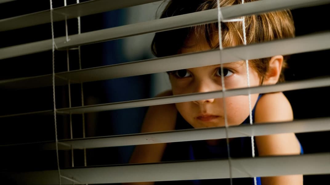 Ein kleiner Junge schaut bei Gewitter ängstlich aus dem Fenster. 