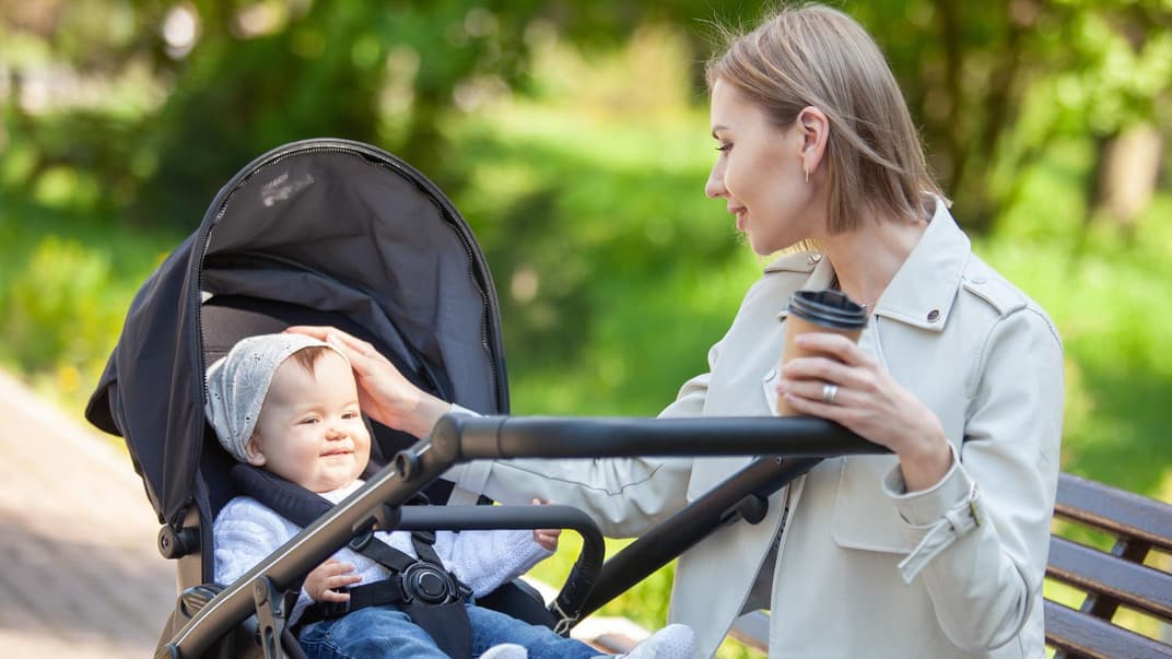 Eine Mutter streichelt ihr Baby im Kinderwagen über den Kopf.