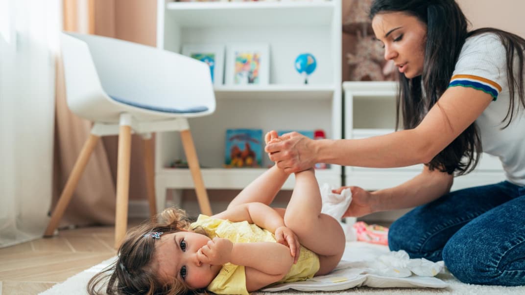 Junge Mutter wickelt ihr Baby auf dem Boden mit Feuchttüchern