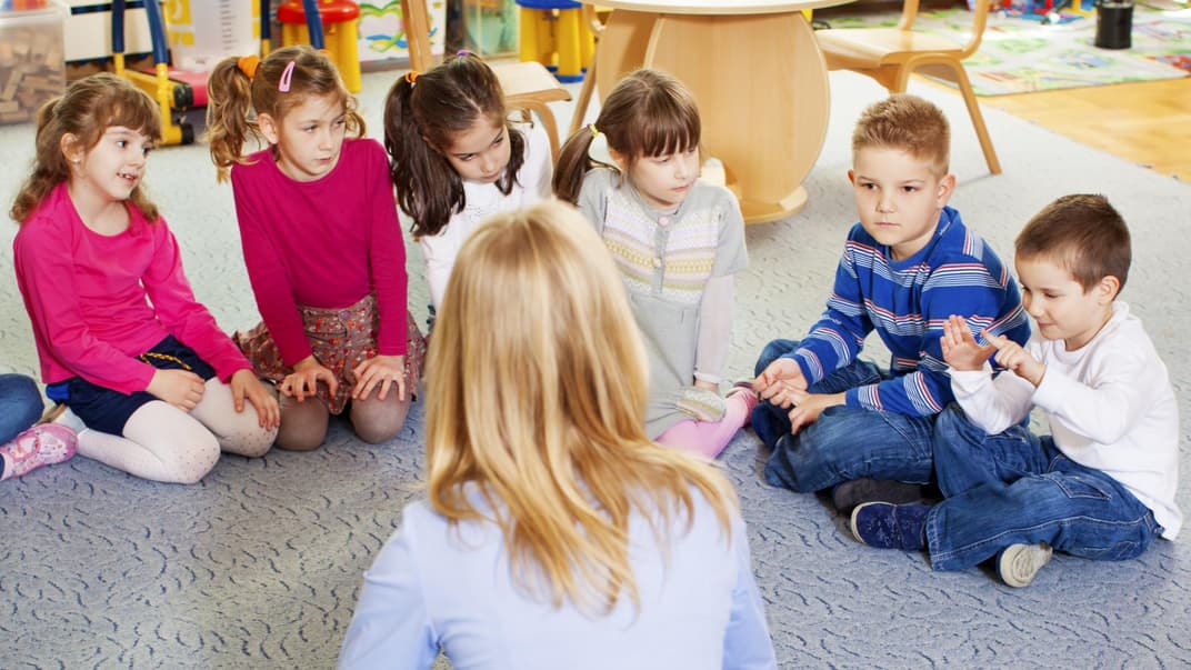 Kinder und Erzieherin sitzen im Kreis.