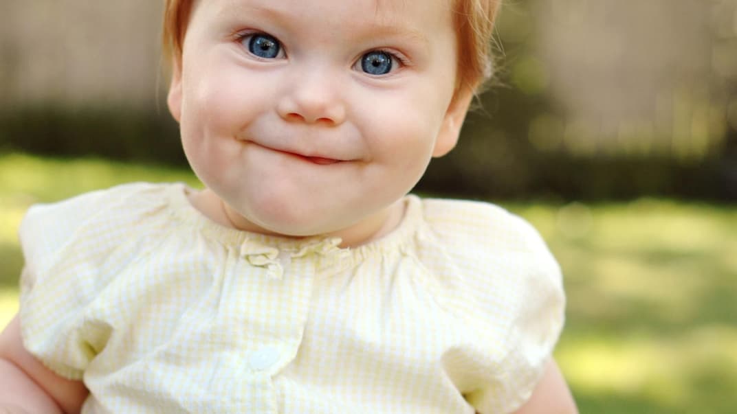 Ein Baby-Mädchen mit roten Haaren lächelt und freut sich über ihren englischen Mädchennamen.