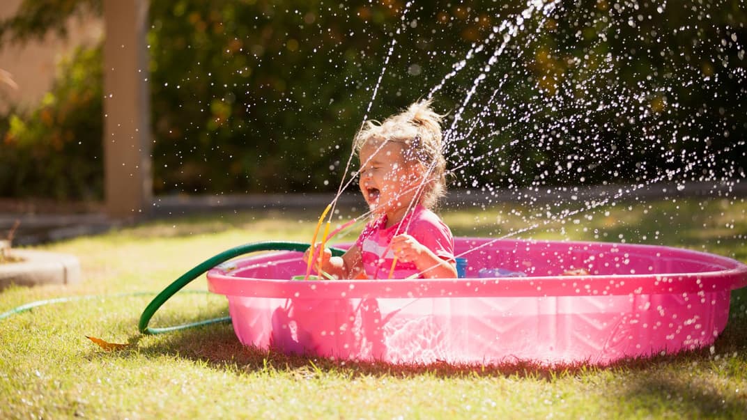 Kleines Mädchen spielt in einem Plantschbecken mit einem Wasserspielzeug.