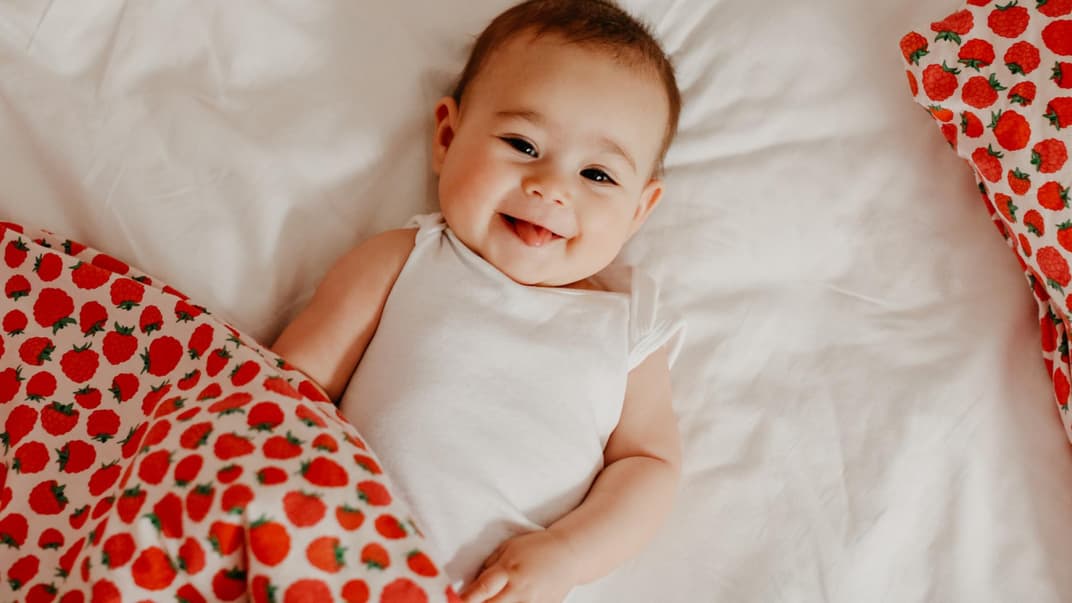 Kleines Baby-Mädchen lacht frech in die Kamera und liegt auf dem Boden.