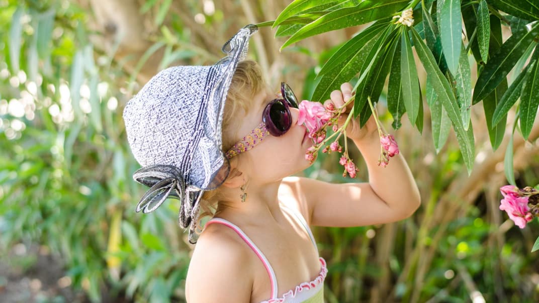 Mädchen mit Hut und Sonnenbrille riecht an einem Blumenstrauch im Garten