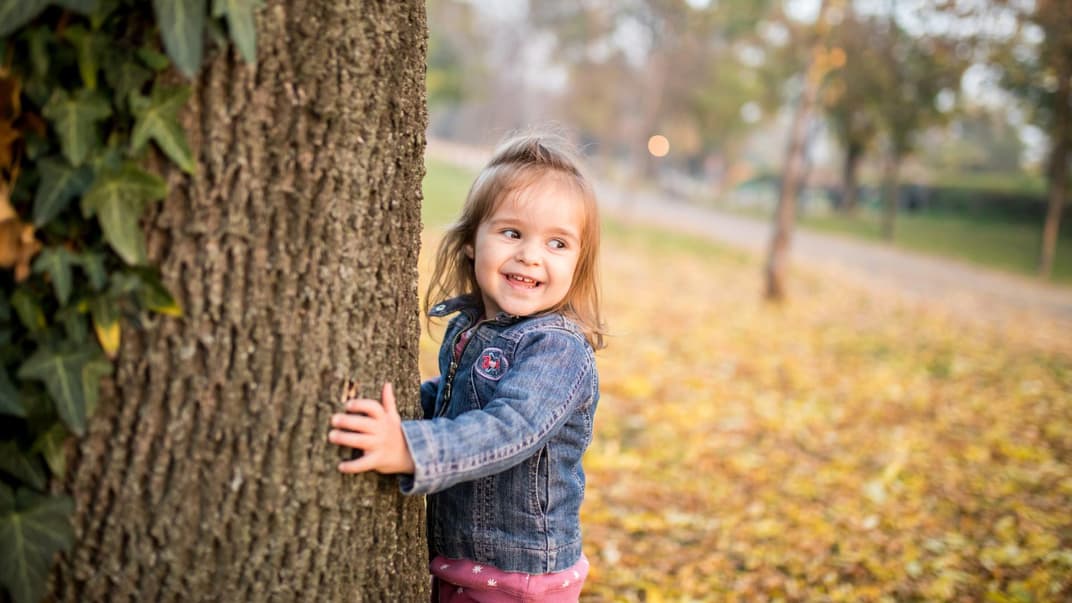Fröhliches Kind läuft um Efeu-berankten Baum