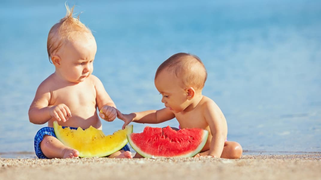 Zwei Babys essen am Strand Melone.