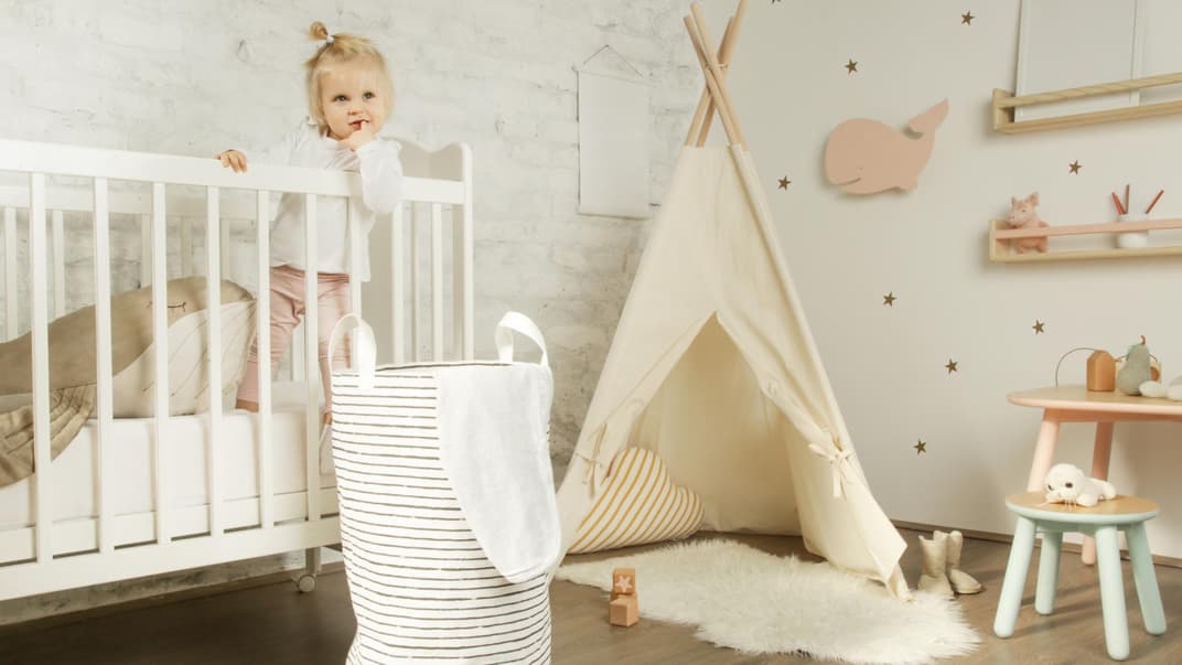 Ein kleines Mädchen steht in ihrem Kinderbett im Kinderzimmer.
