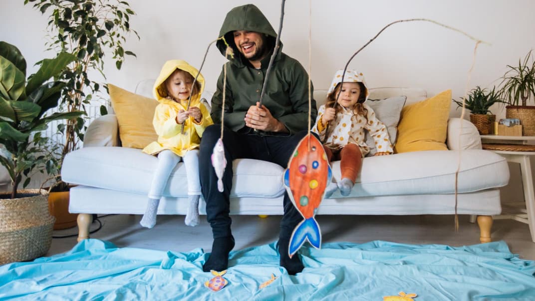 Vater spielt mit seinen Töchtern Angeln auf dem Sofa. 