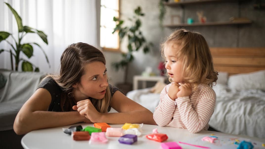 Mutter spricht mit ihrer kleinen Tochter am Spieltisch.
