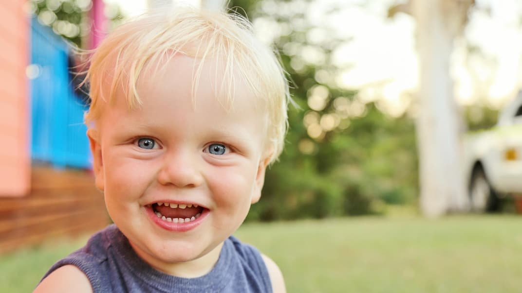 Kleiner, blonder Junge strahlt in die Kamera.