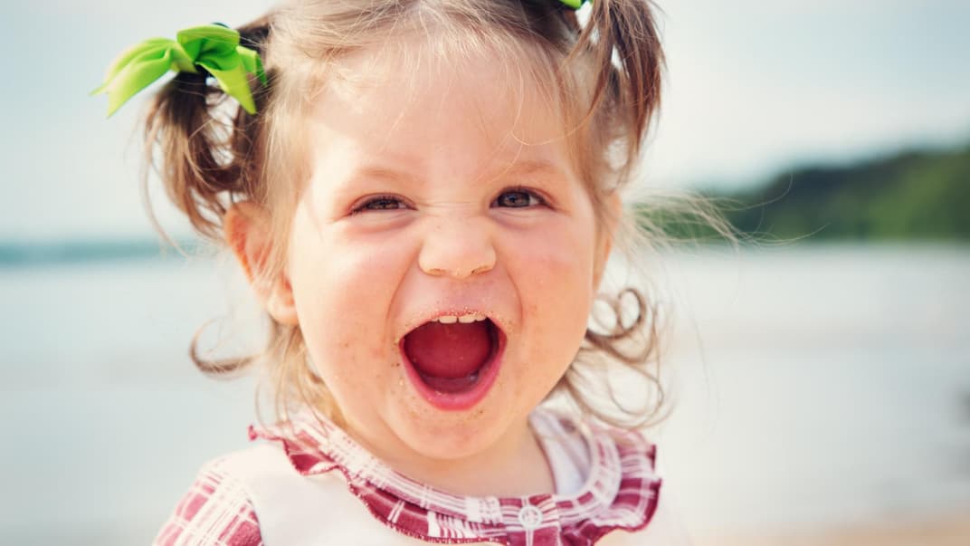 Kleines niedliches Baby-Mädchen lacht am Strand und freut sich über ihren starken Namen.