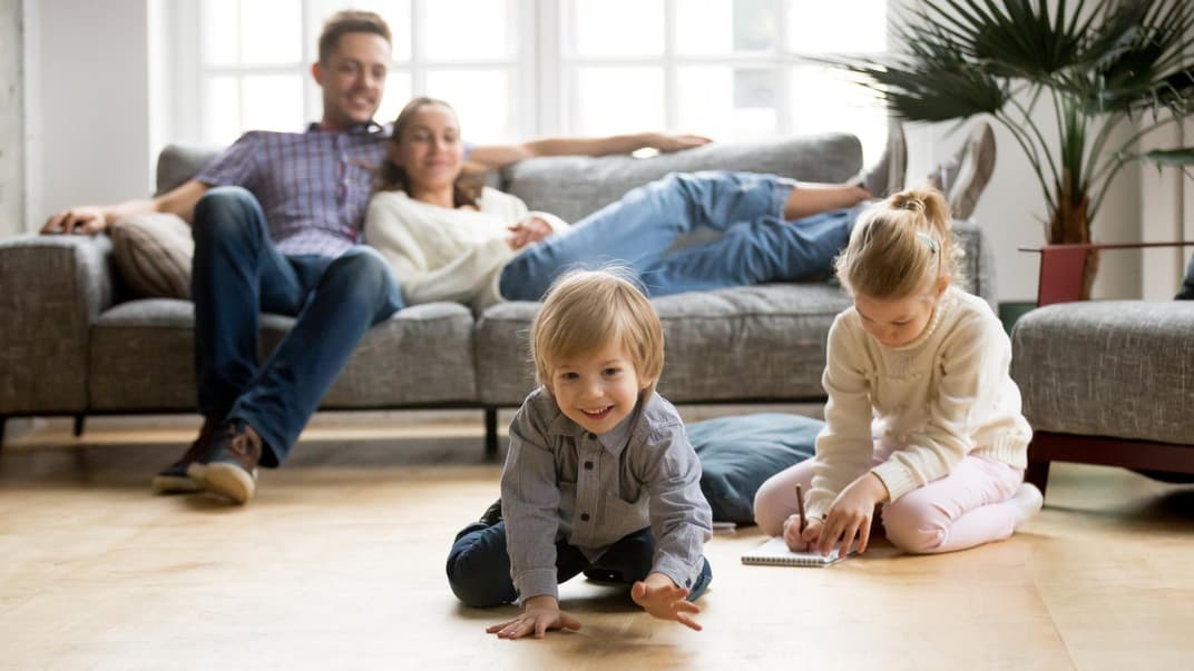 Kinder spielen, Eltern sitzen entspannt auf dem Sofa.