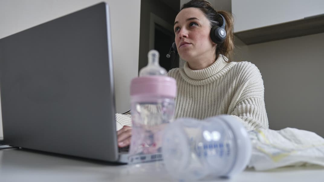 Mutter sitzt mit Milchflaschen und Windeln am Laptop.