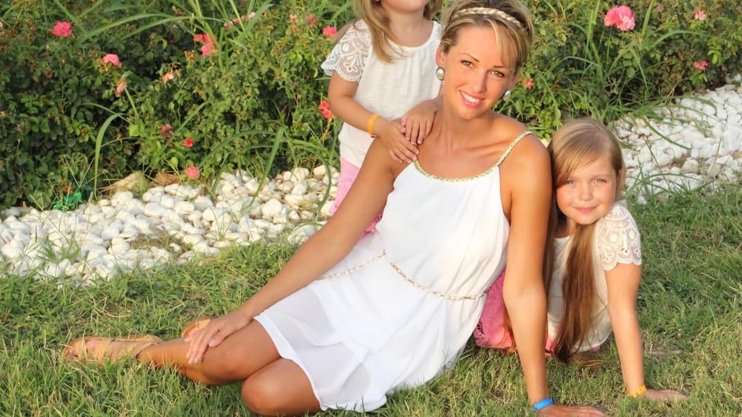 Mutter sitzt mit ihren zwei Töchtern auf dem Rasen.