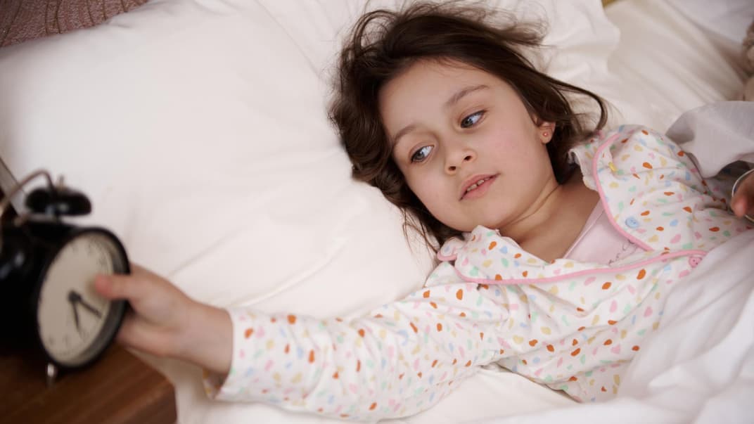 Mädchen liegt im Bett und stellt ihren Wecker aus.