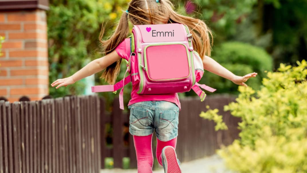 Mädchen mit einem bestickten Schulranzen läuft den Gehweg entlang.