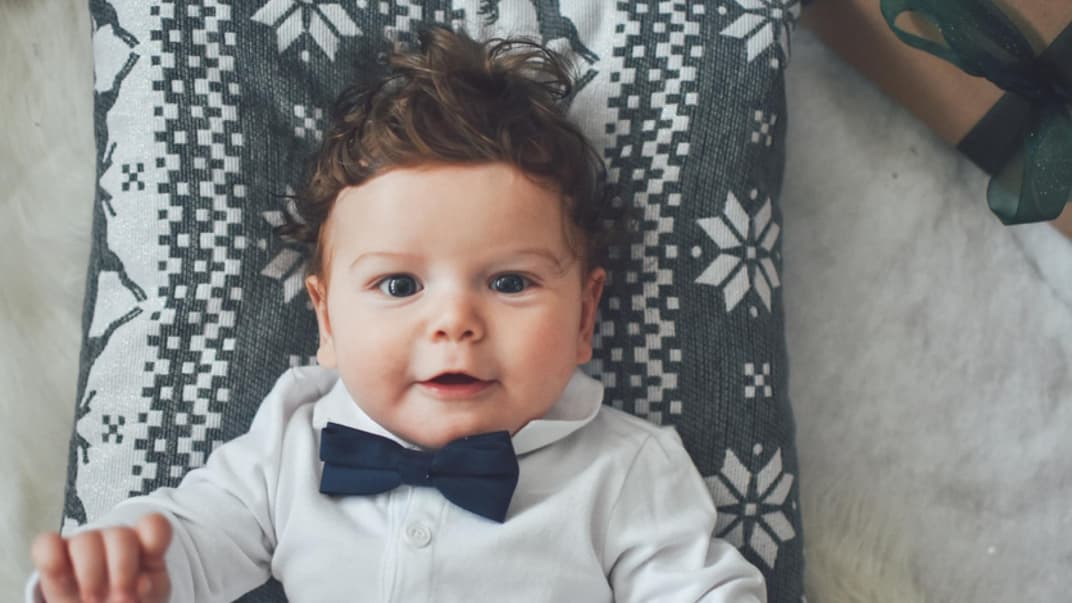 Kleiner Junge mit Fliege lächelt auf einem Kissen liegend in die Kamera.