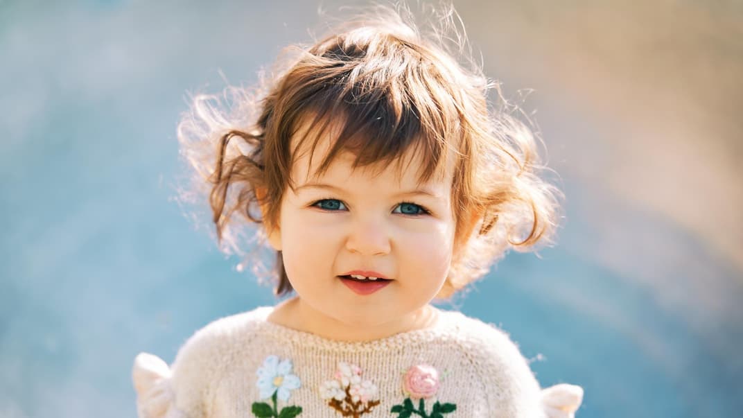 Ein kleines Mädchen mit lockigem Haar schaut in die Kamera.