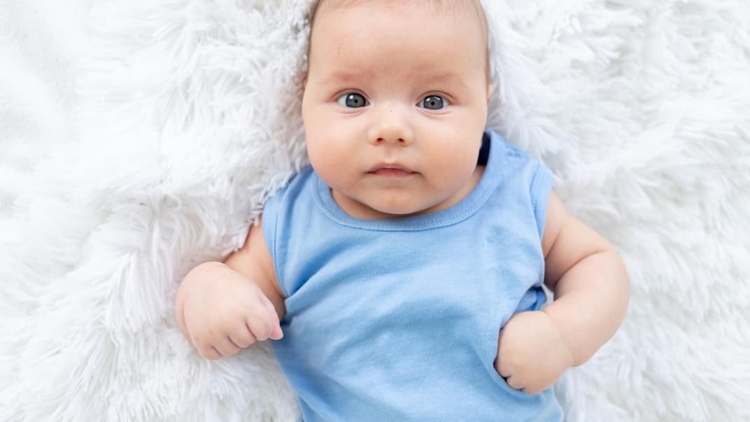 Baby-Junge in einem blauen Body liegt auf einem Lammfell