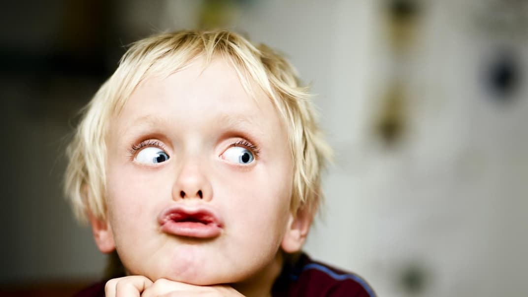 Kleiner, frecher Junge mit blondem Haar sieht eine Grimasse. 