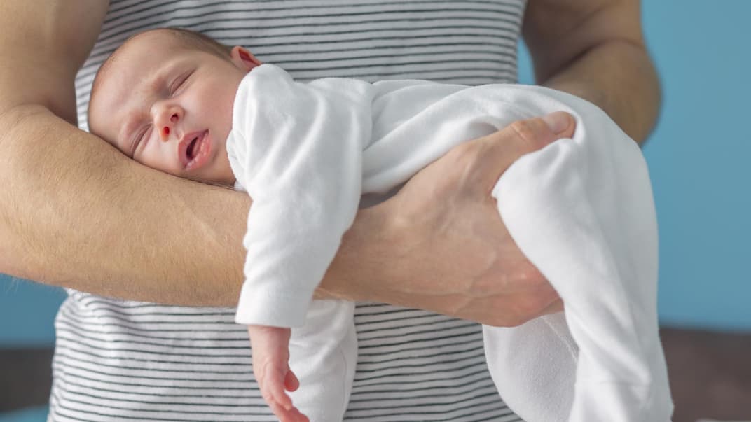 Ein Vater hält sein Neugeborenes im Fliegergriff vor seinem Bauch