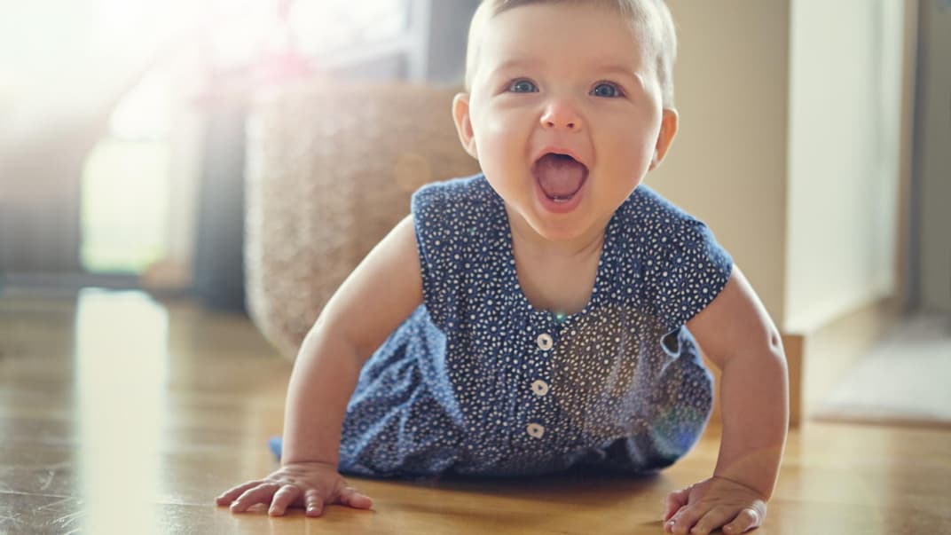 Baby-Mädchen robbt auf dem Boden und lacht mit offenen Mund.