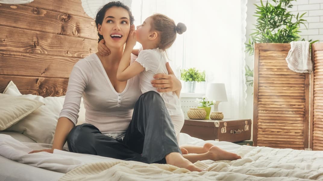 Mädchen flüstert seiner Mama etwas ins Ohr.