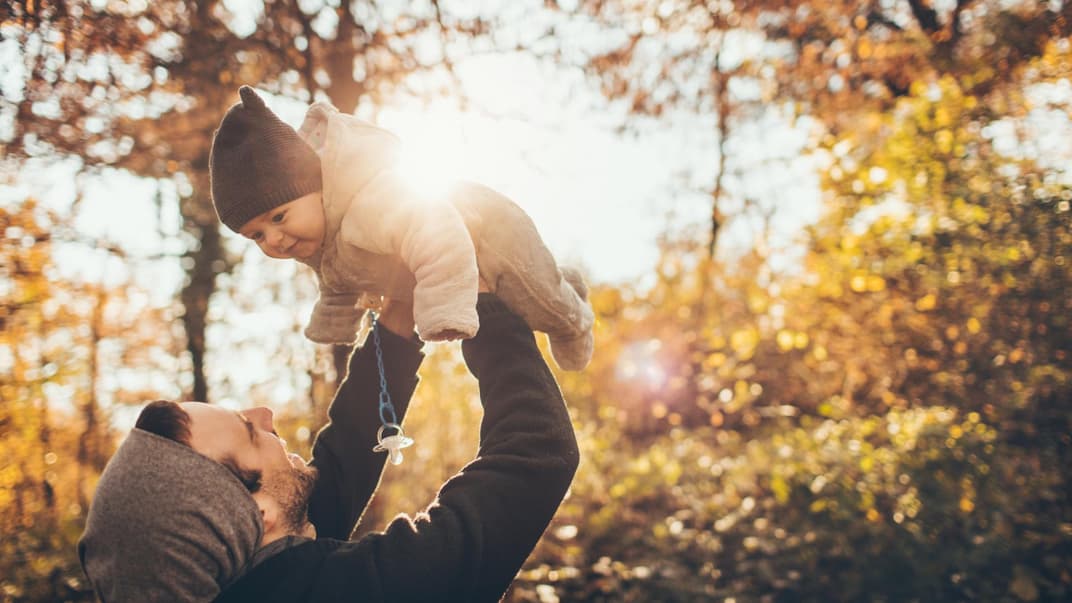 Papa hält Baby hoch im herbstlichen Wald