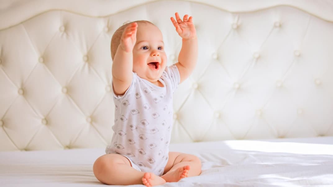 Baby sitzt lachend auf dem Bett.