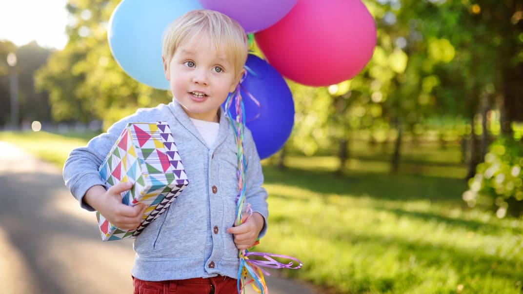 Kleiner blonder Junge feiert 3 Geburtstag und trägt Ballon und Geschenk. 