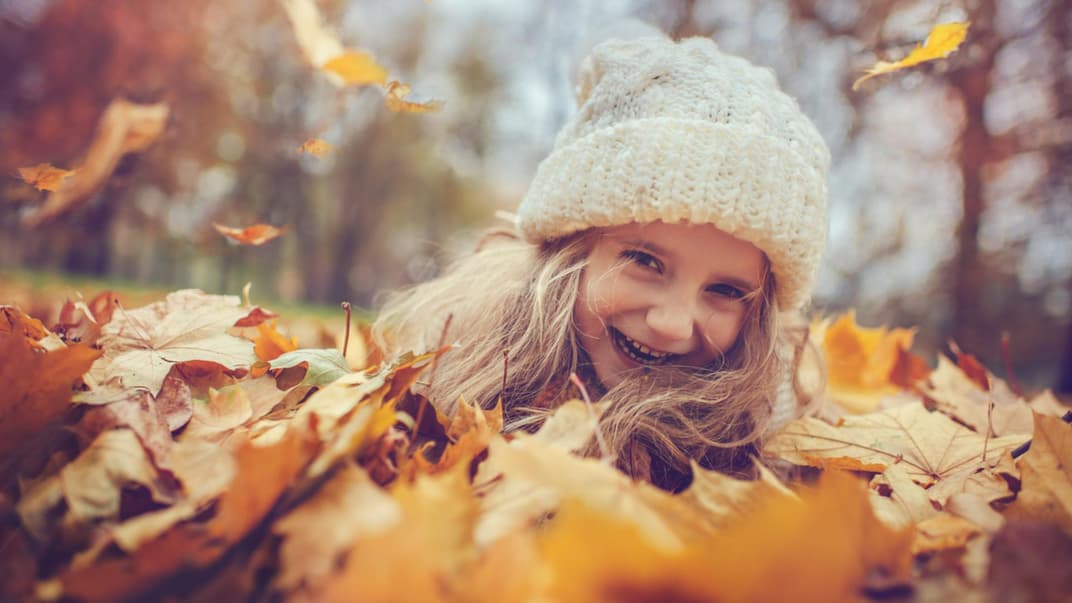Mädchen mit Mütze im Herbstlaub.