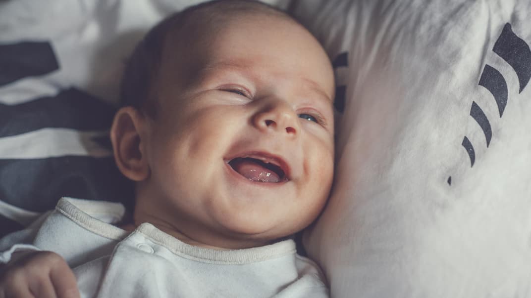 Kleiner Baby-Junge lacht zufrieden und liegt auf dem Bett. 