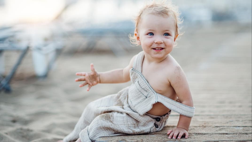 Ein kleines Mädchen sitzt mit Sand an den Händen am Strand.