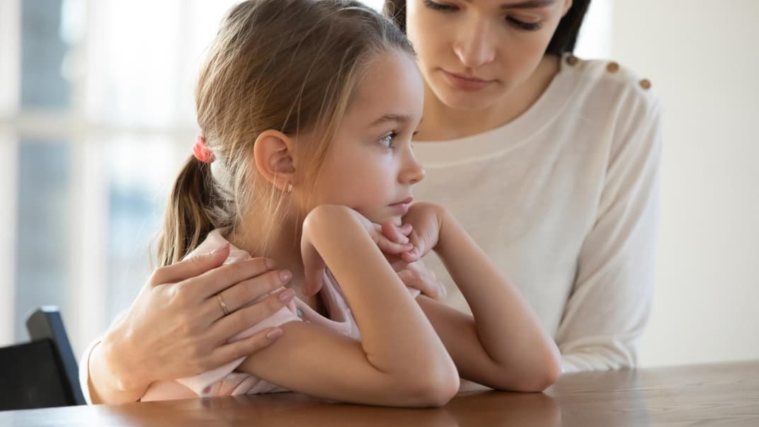 Mutter legt den Arm um ihr trauriges Kind.