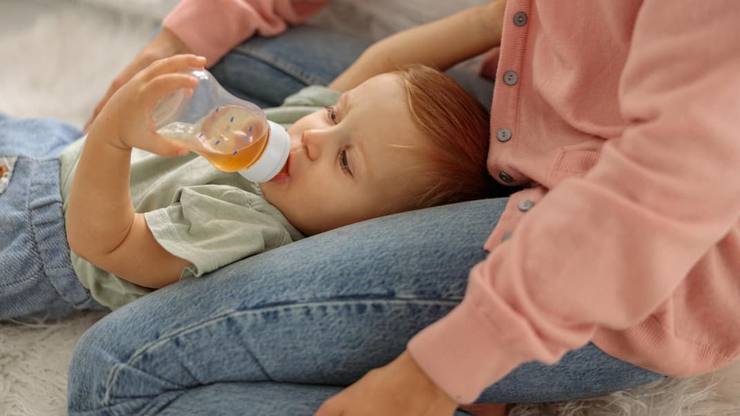 Ein kleiner Baby-Junge trinkt liegend Fencheltee aus einer Nuckelflasche. 