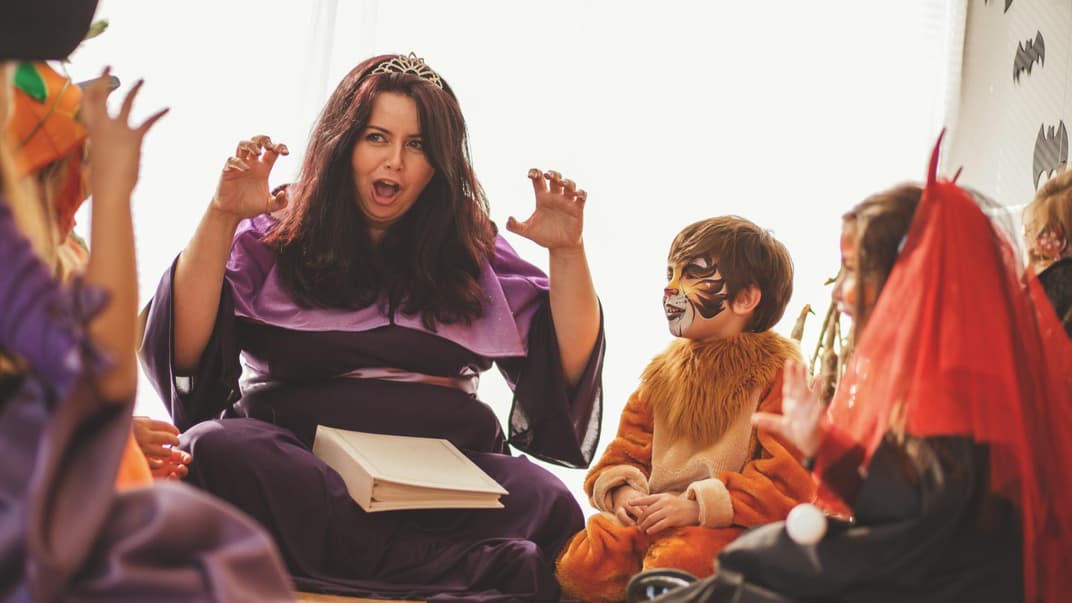 Eine verkleidete Frau liest den verkleideten Kindern eine Gruselgeschichte vor.
