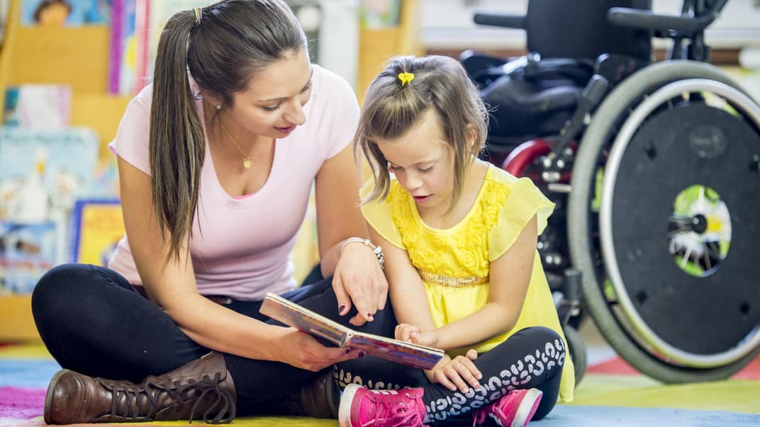 Eine Frau schaut sich gemeinsam mit meinem Mädchen im Rollstuhl ein Buch an.