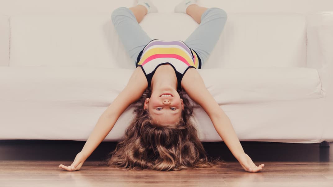 Kleines Mädchen Kind mit langen Haaren kopfüber auf dem Sofa.
