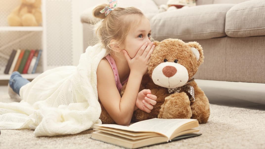 Kleines Mädchen flüstert ihrem Teddy ein Geheimnis ins Ohr.