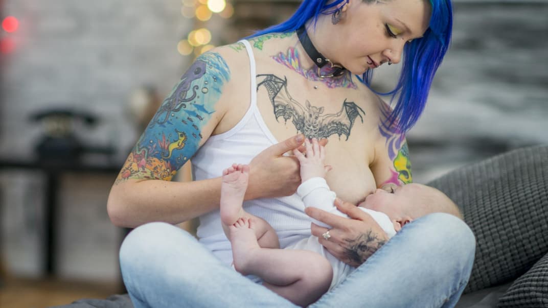 Tätowierte Frau stillt ihr Baby.